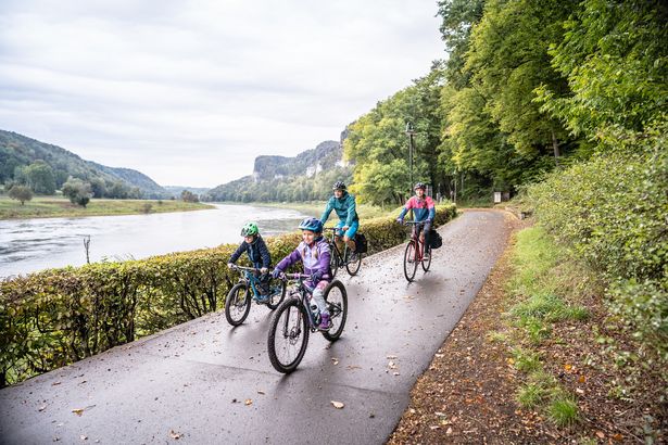 Eine Familie radelt auf einem Radweg an der Elbe entlang.