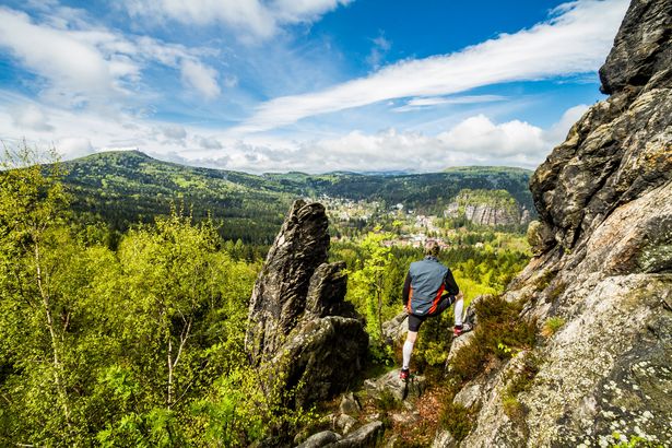 Ein Wanderer auf dem Oberlausitzer Bergweg steht auf einem Felsen und schaut in die Landschaft. 