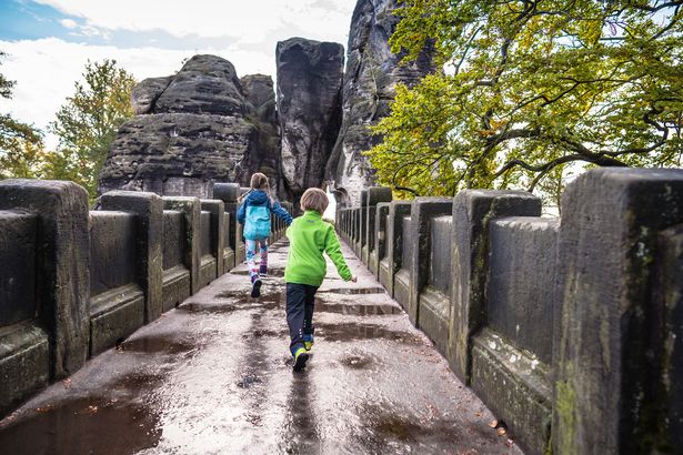 Zwei Kinder rennen über eine Brücke im Nationalpark Sächsische Schweiz. Dahinter erheben sich die Sandsteinfelsen des Nationalparks.